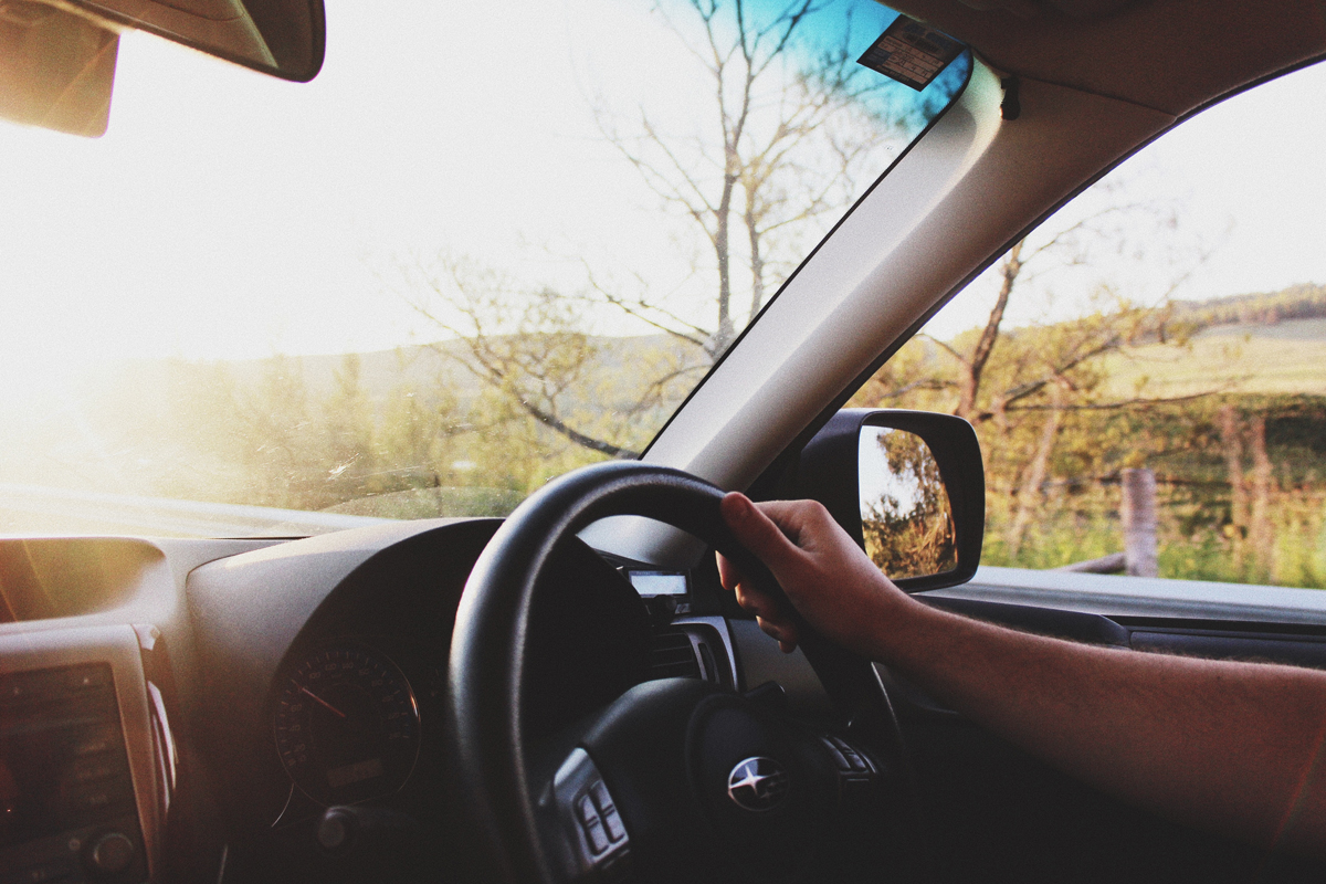 A person driving a car with the sun setting in the background