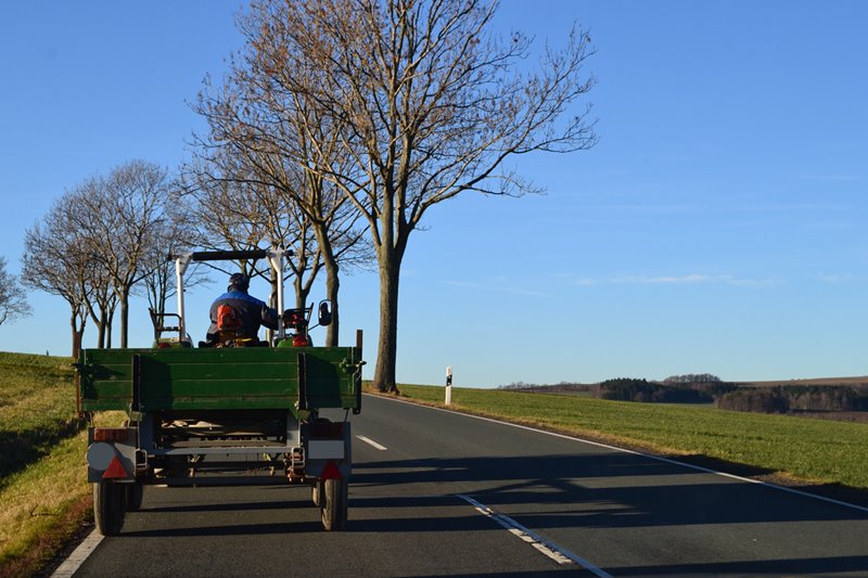 A farm tractor with a trailer attached driving along a country road