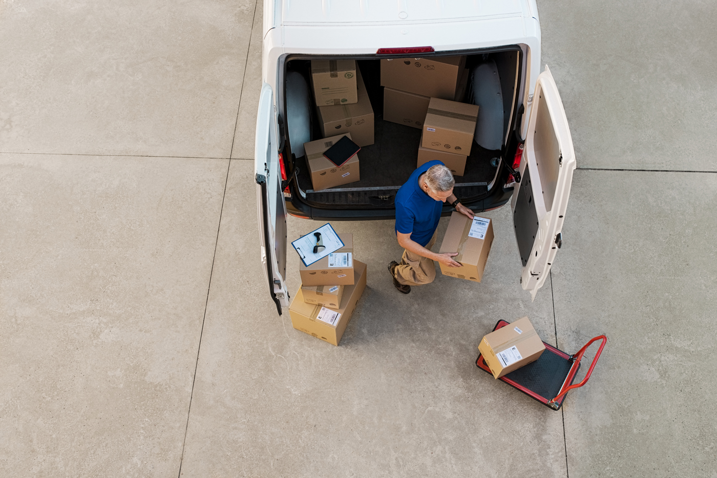 A courier unloading packages from his van with a dolly