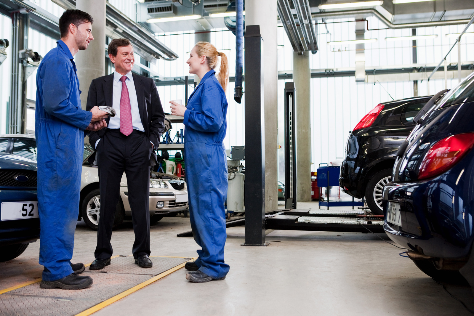 A motor trade business owner talking to two employee's in a car workshop
