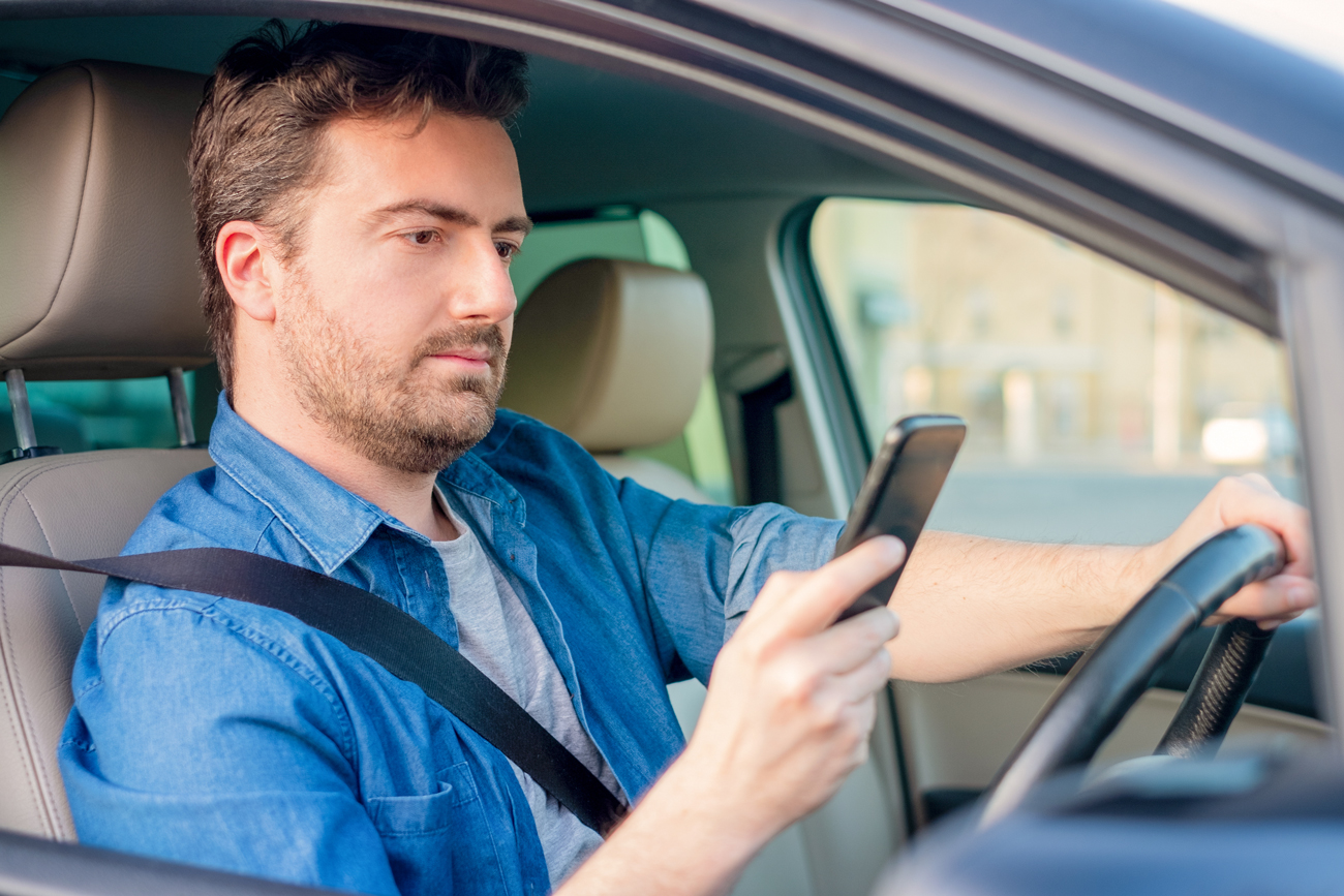 A man using his phone with one hand while driving