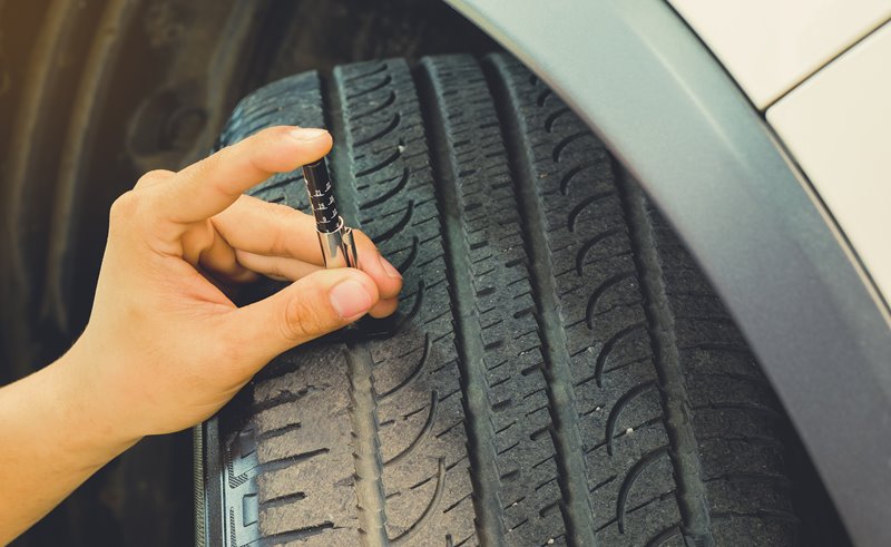Driver checking tyre tread depth using tool