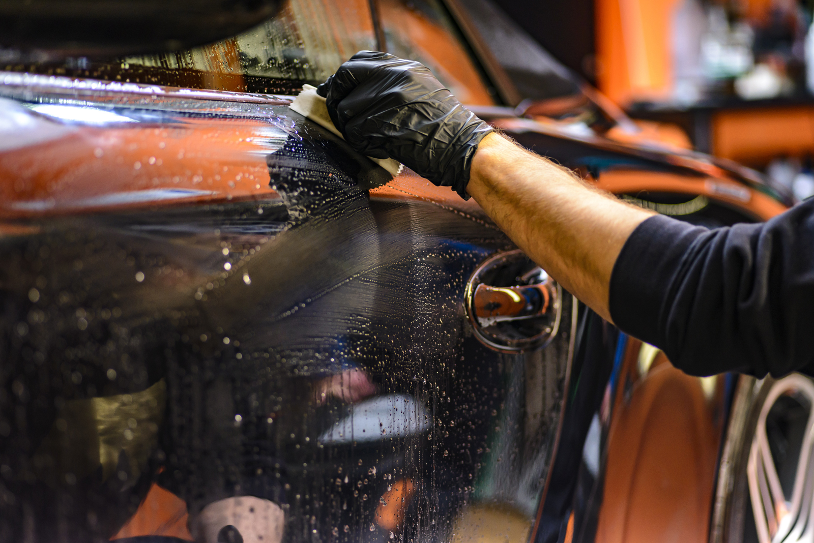 A mechanic wearing gloves cleaning the side of a reconditioned car