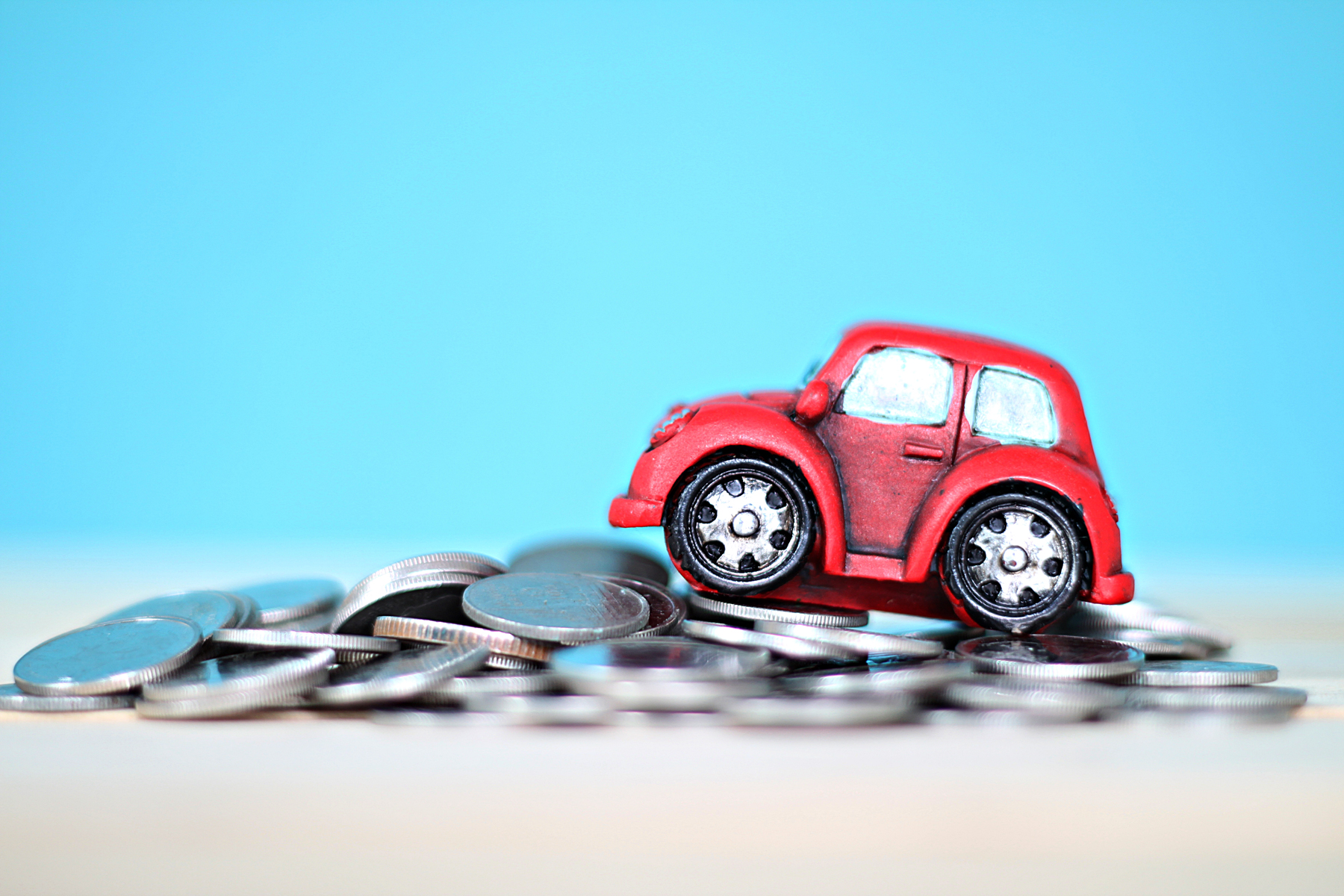 A model car placed on-top of a pile of coins against a blue background