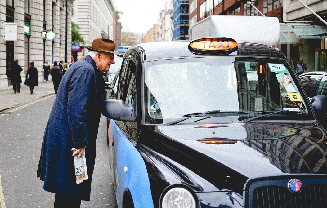 A man talking to a taxi driver through the taxi's window