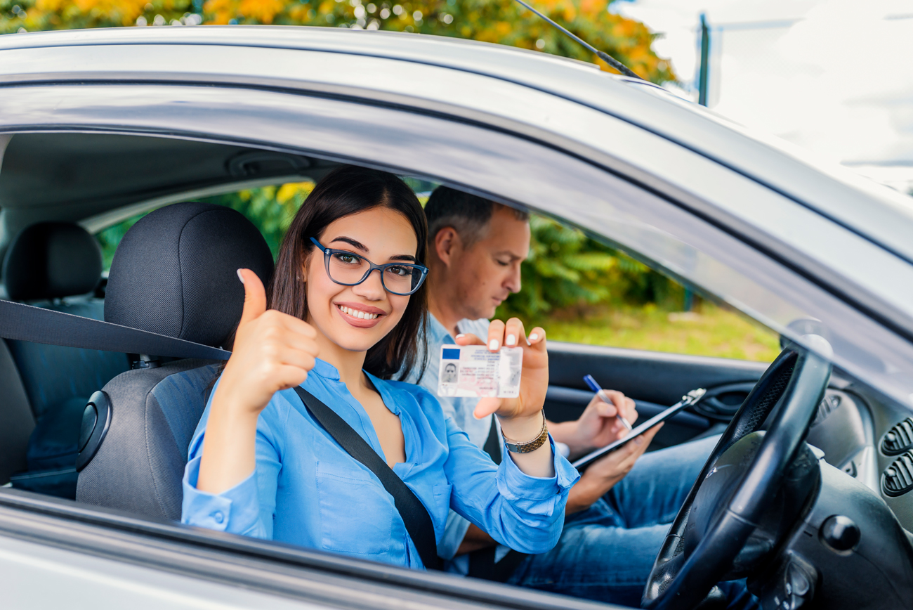 A young driver sitting in a car holding her driving license up