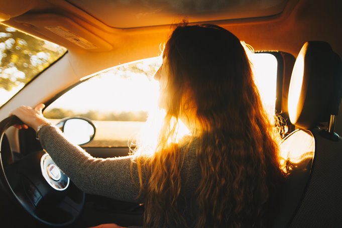 A woman driving on a country road with the sunsetting behind