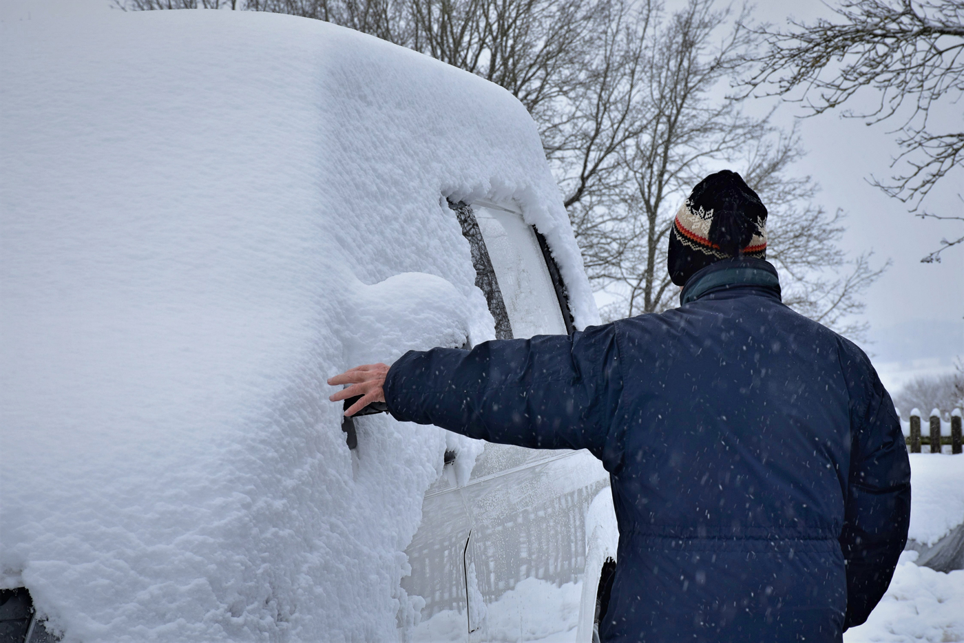 A man in winter clothing assessing the snow on his van