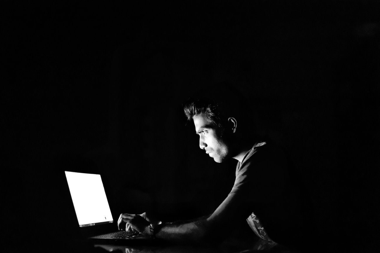 A person sitting using a laptop suspiciously in a dark room