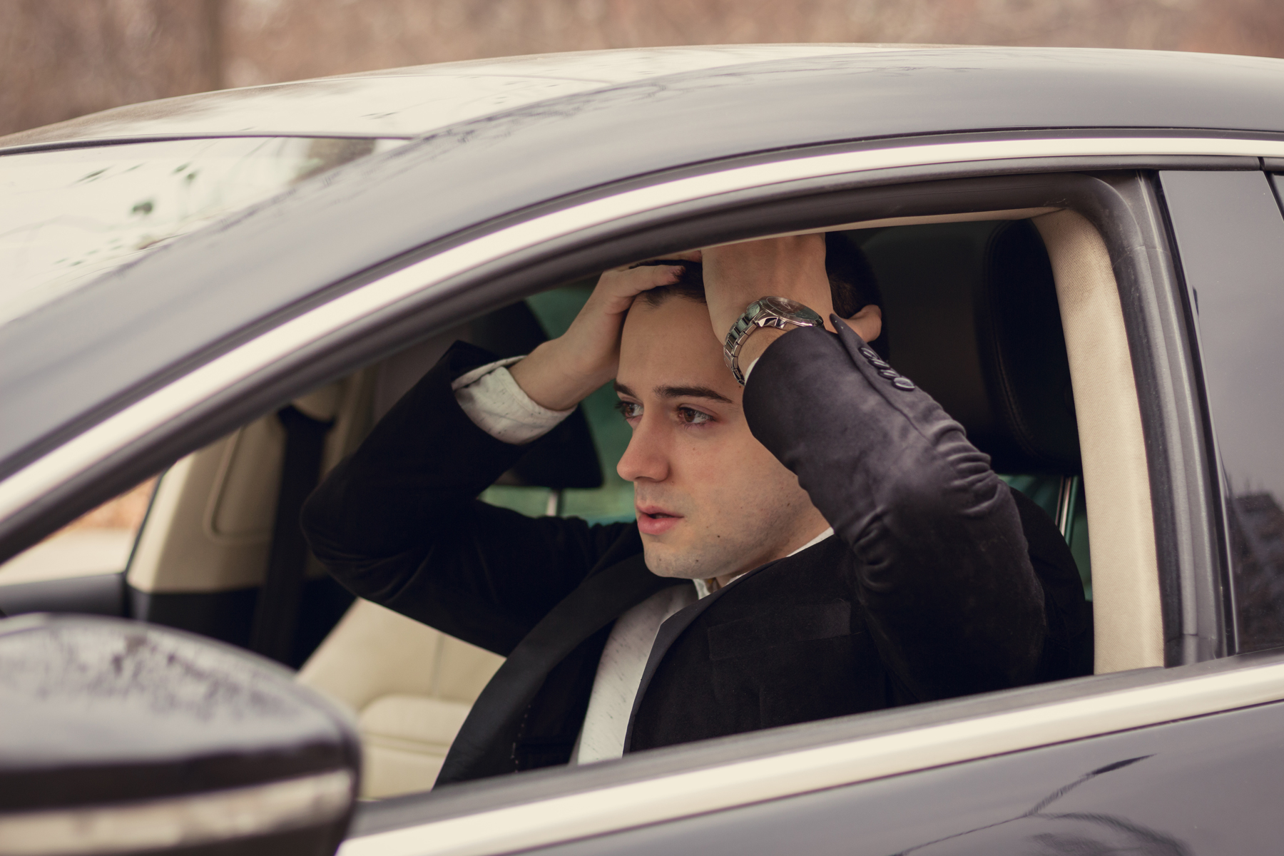A distressed man with his hands on his head sitting in his car