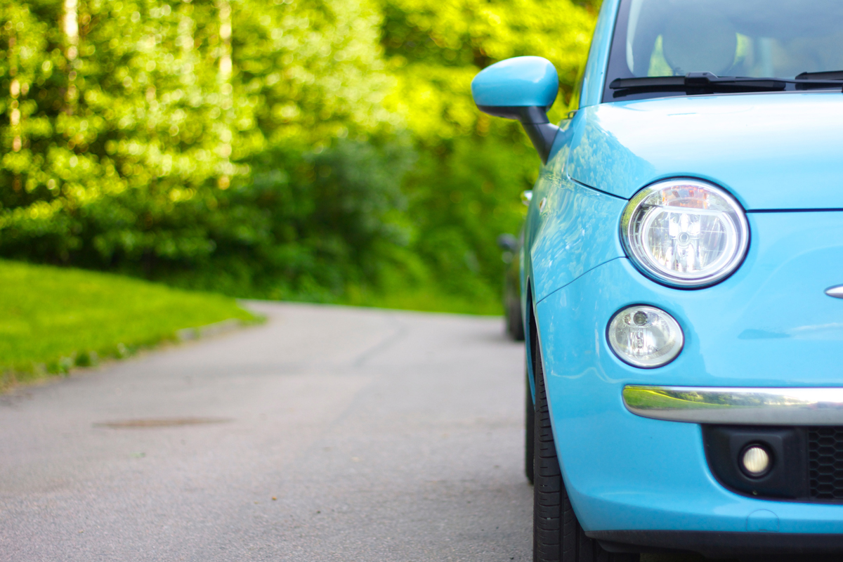 A blue Fiat parked on a long driveway in the countryside