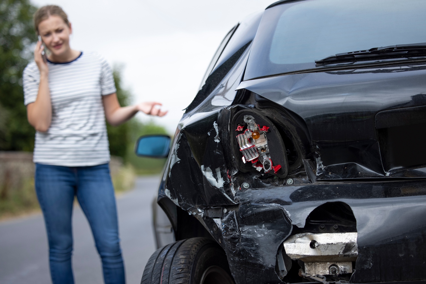 A woman on her mobile phone looking at her damaged car after a crash