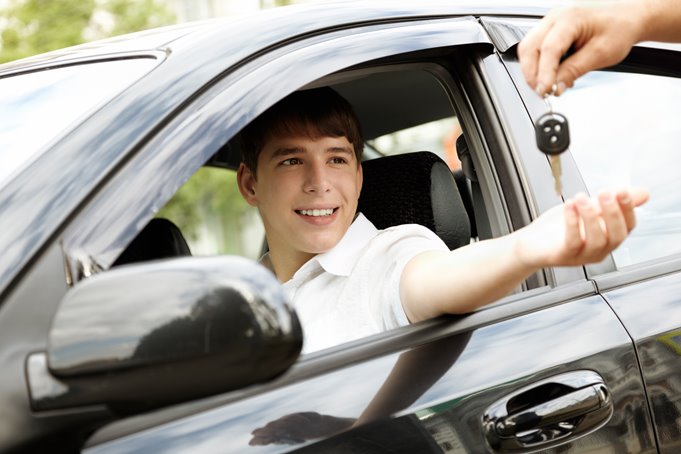 A young man sitting in a car being handed the keys