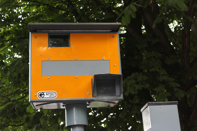 A speed camera in-front of a tree on a road